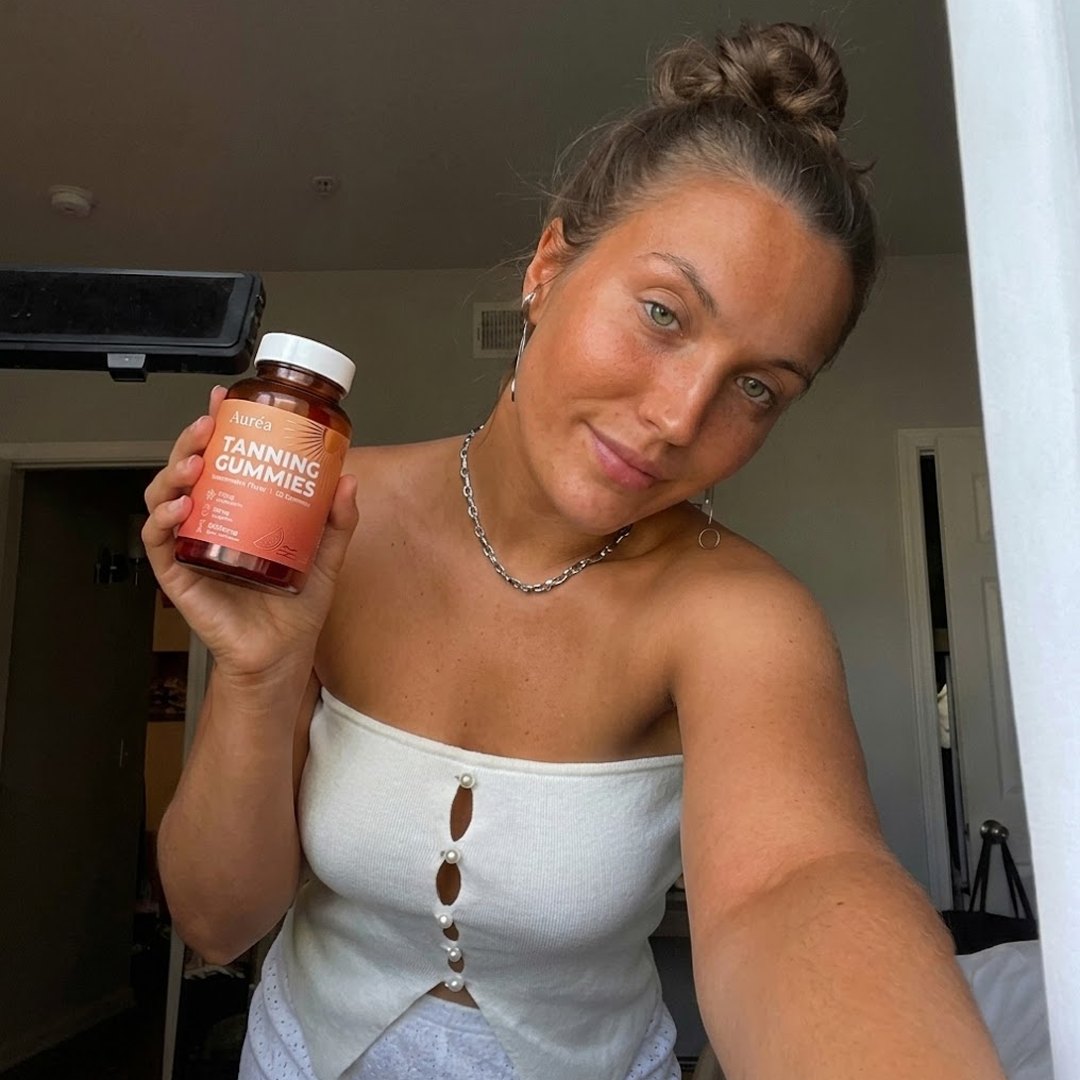 Hand holding a jar of Auréa Tanning Gummies